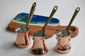 Three copper coffee pots with brass handles on a white surface.