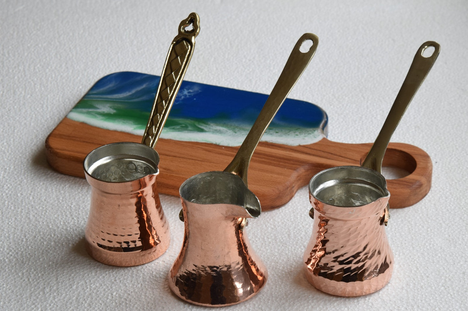 Three copper coffee pots with brass handles on a white surface.