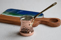 Copper Turkish coffee pot with a wooden handle on a white surface