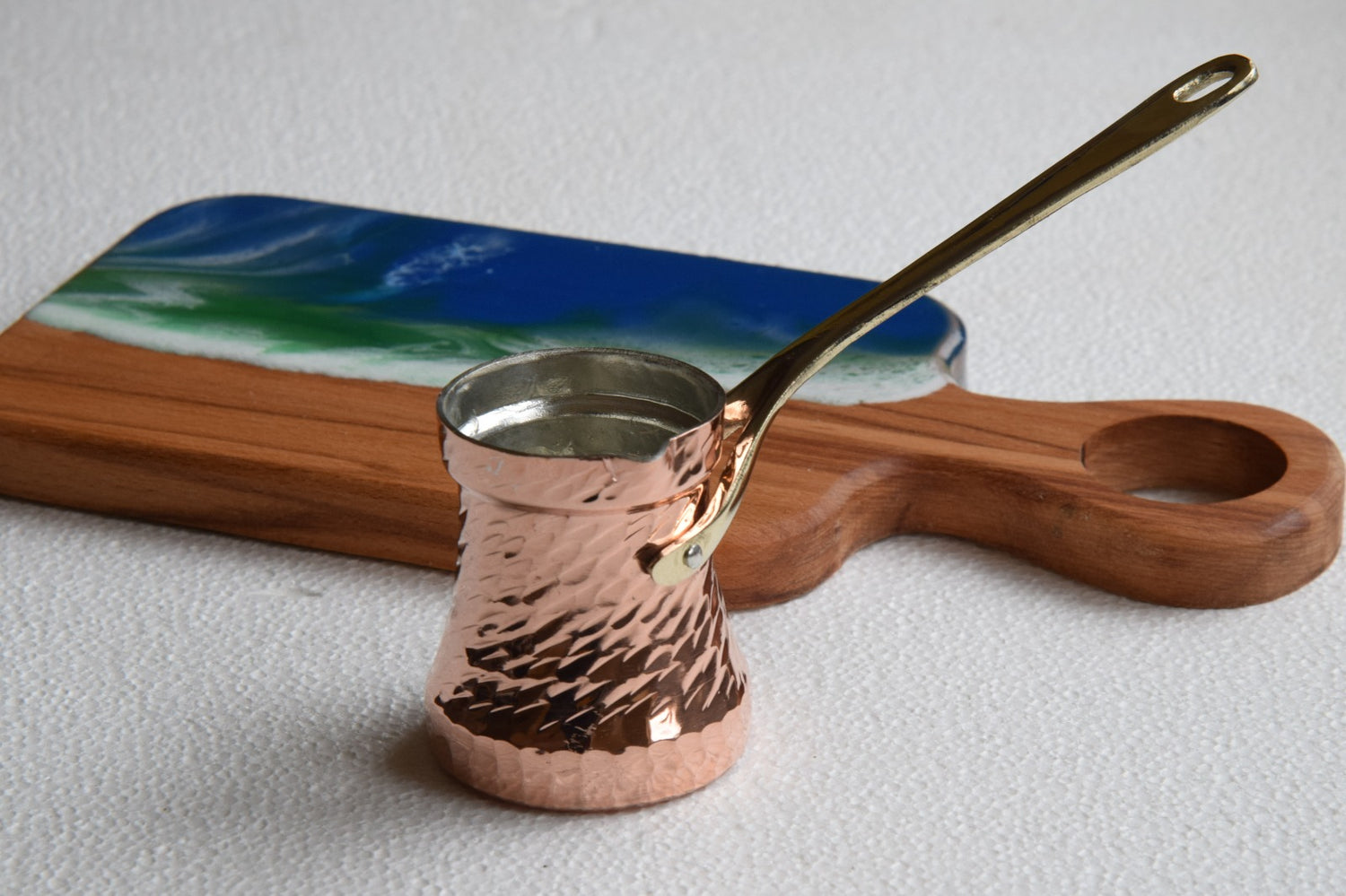 Copper Turkish coffee pot with a wooden handle on a white surface