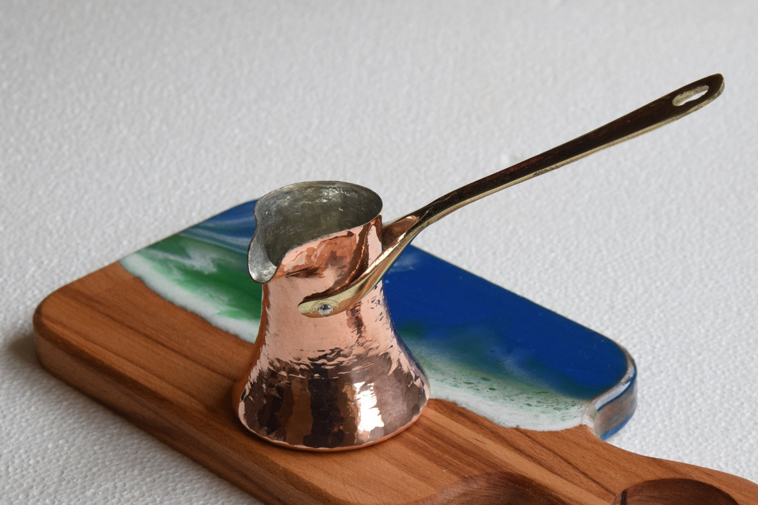 Copper Turkish coffee pot on a wooden stand with a scenic design